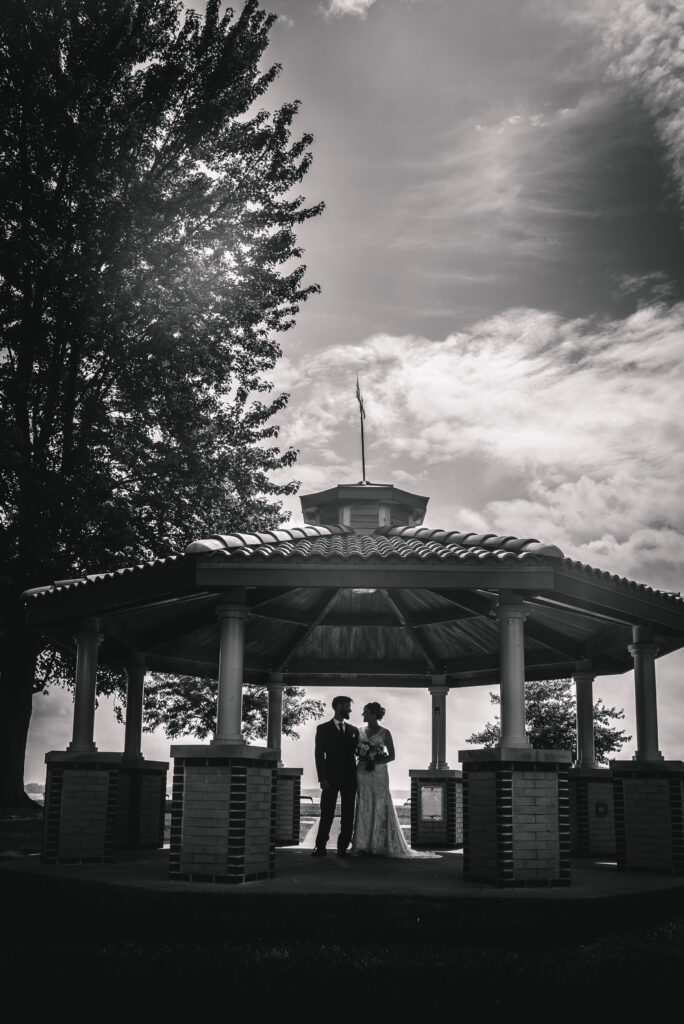 Wedding couple in lake geneva in black and white in a gazebo by a lake