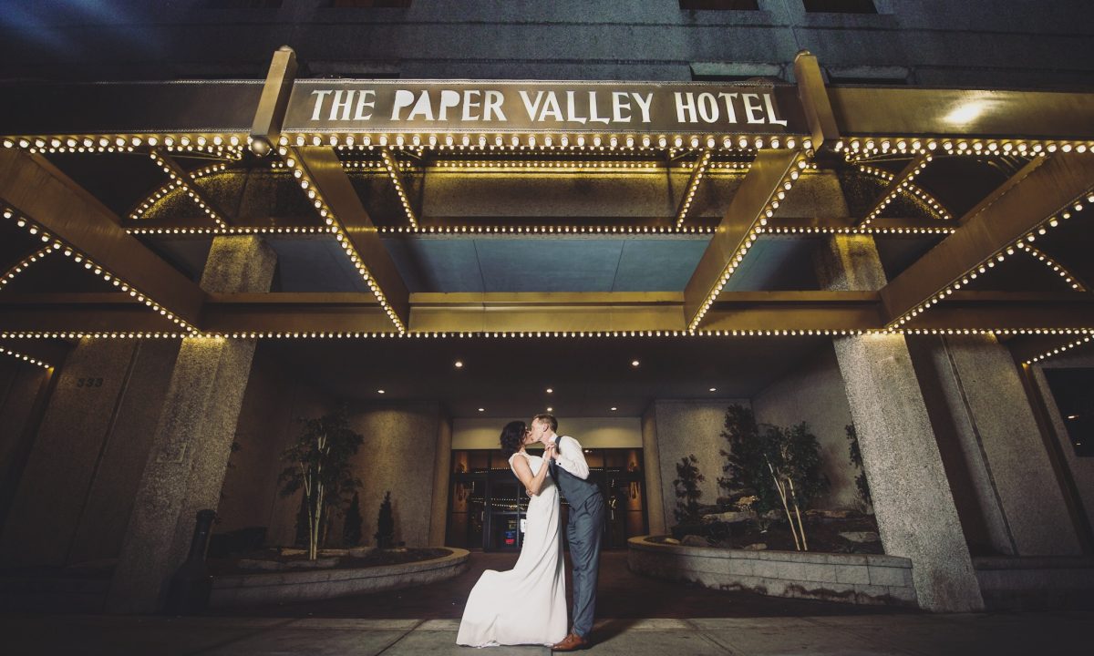 Couple in front of Paper Valley Hotel in fox valley on their wedding day kissing.